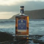 Bouteille de whisky Aerstone Sea Cask 10 ans sur côte rocheuse avec vagues et ciel brumeux