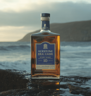 Bouteille de whisky Aerstone Sea Cask 10 ans sur côte rocheuse avec vagues et ciel brumeux