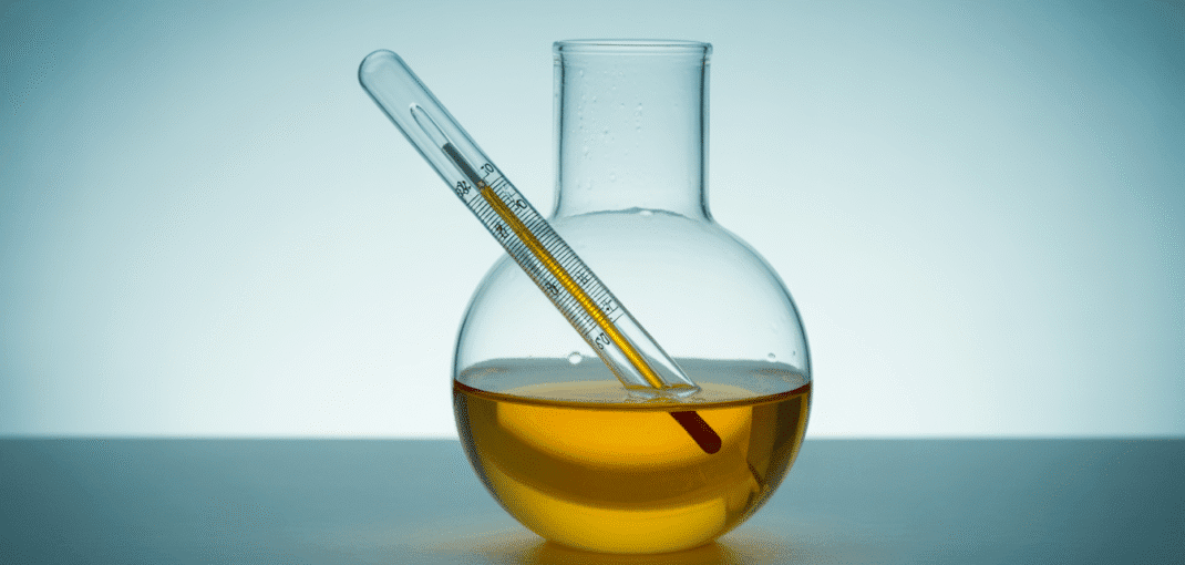 Alcohol hydrometer floating in a transparent liqueur sample inside a glass cylinder with liquid meniscus, lab setting